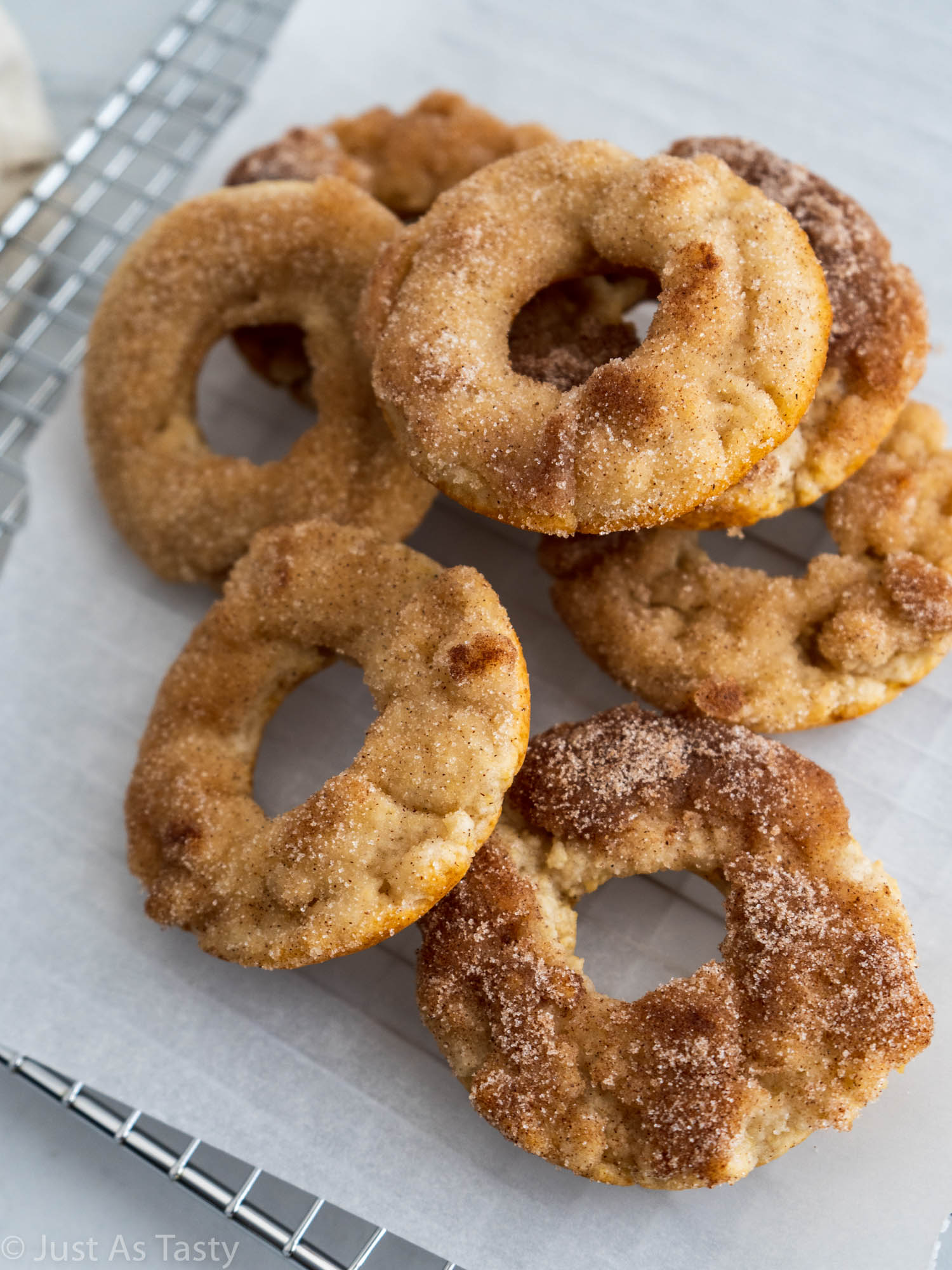 Baked donuts piled onto white parchment paper. 