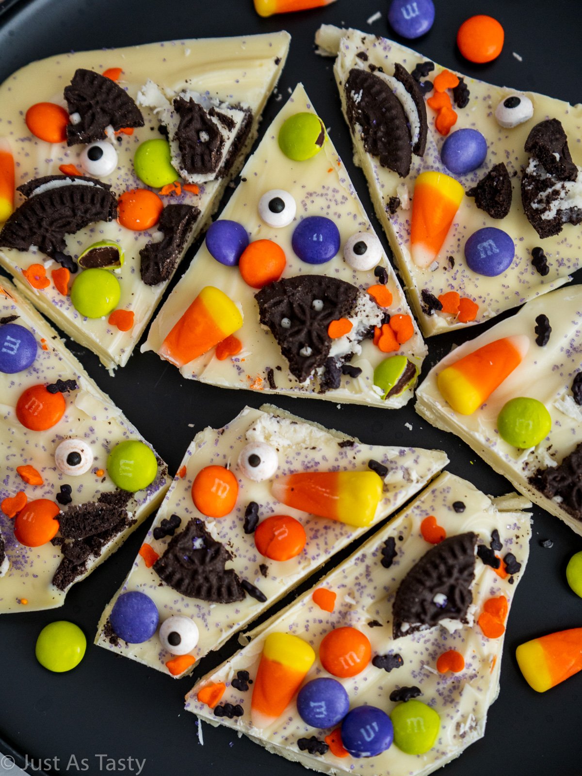 Pieces of white chocolate Halloween bark topped with candy on a black plate.