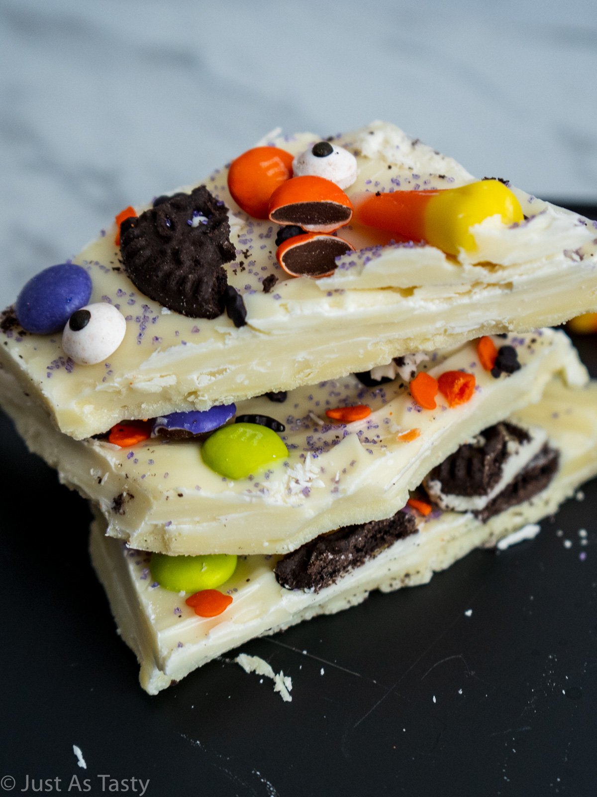 Stack of three pieces of Halloween chocolate bark topped with candy and sprinkles.