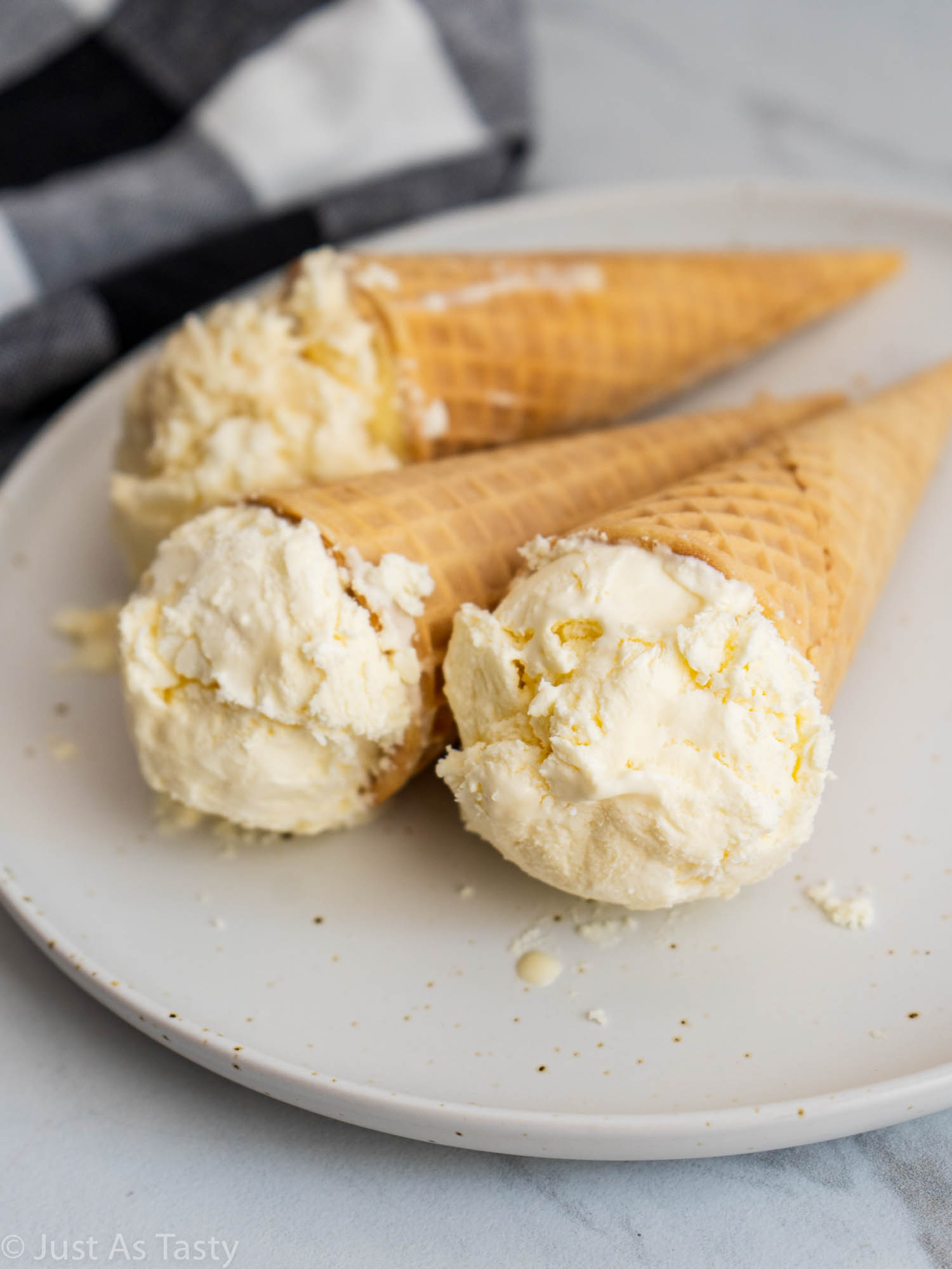 Three ice cream cones, each with a scoop of ice cream, on a white plate.