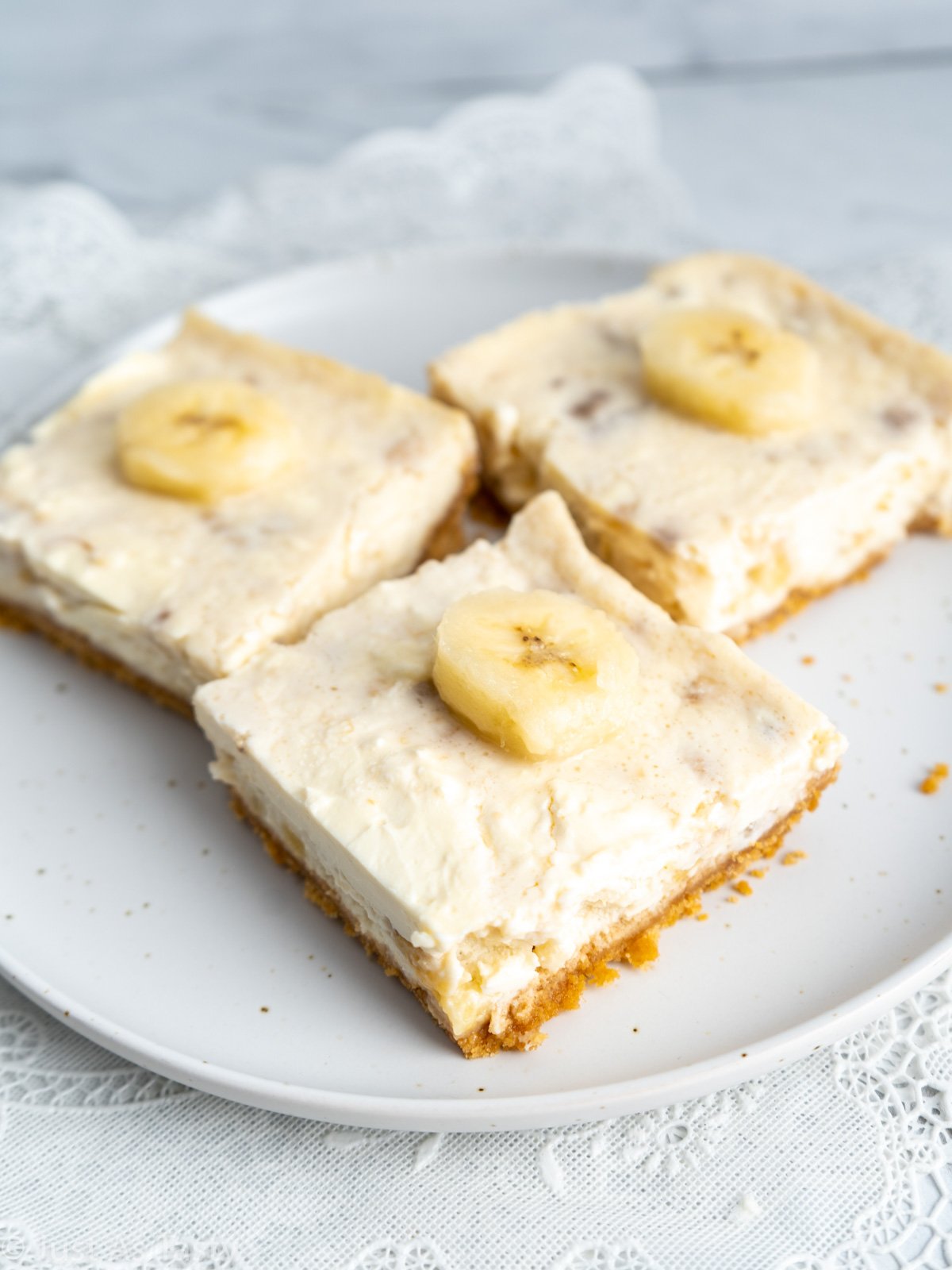 Three banana cheesecake bars on a white plate.