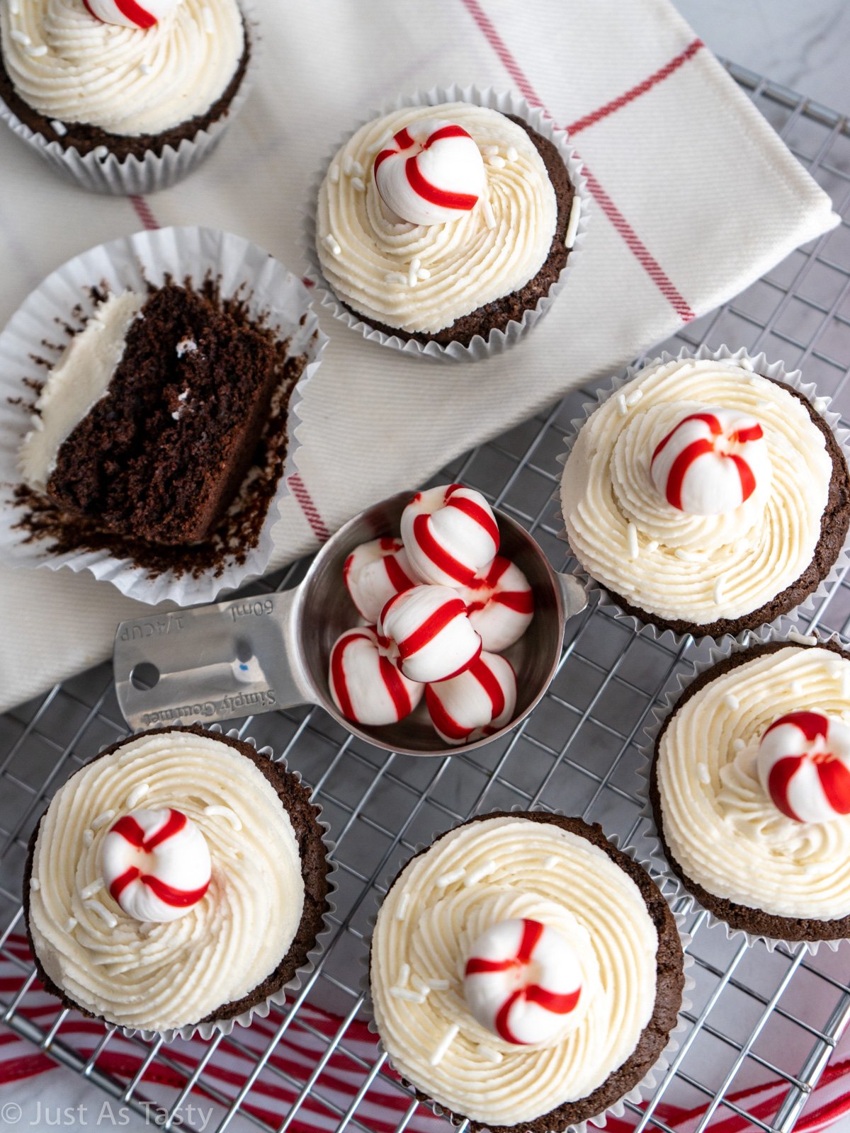 Frosted chocolate cupcakes, topped with red and white striped mints, on a wire cooling rack.