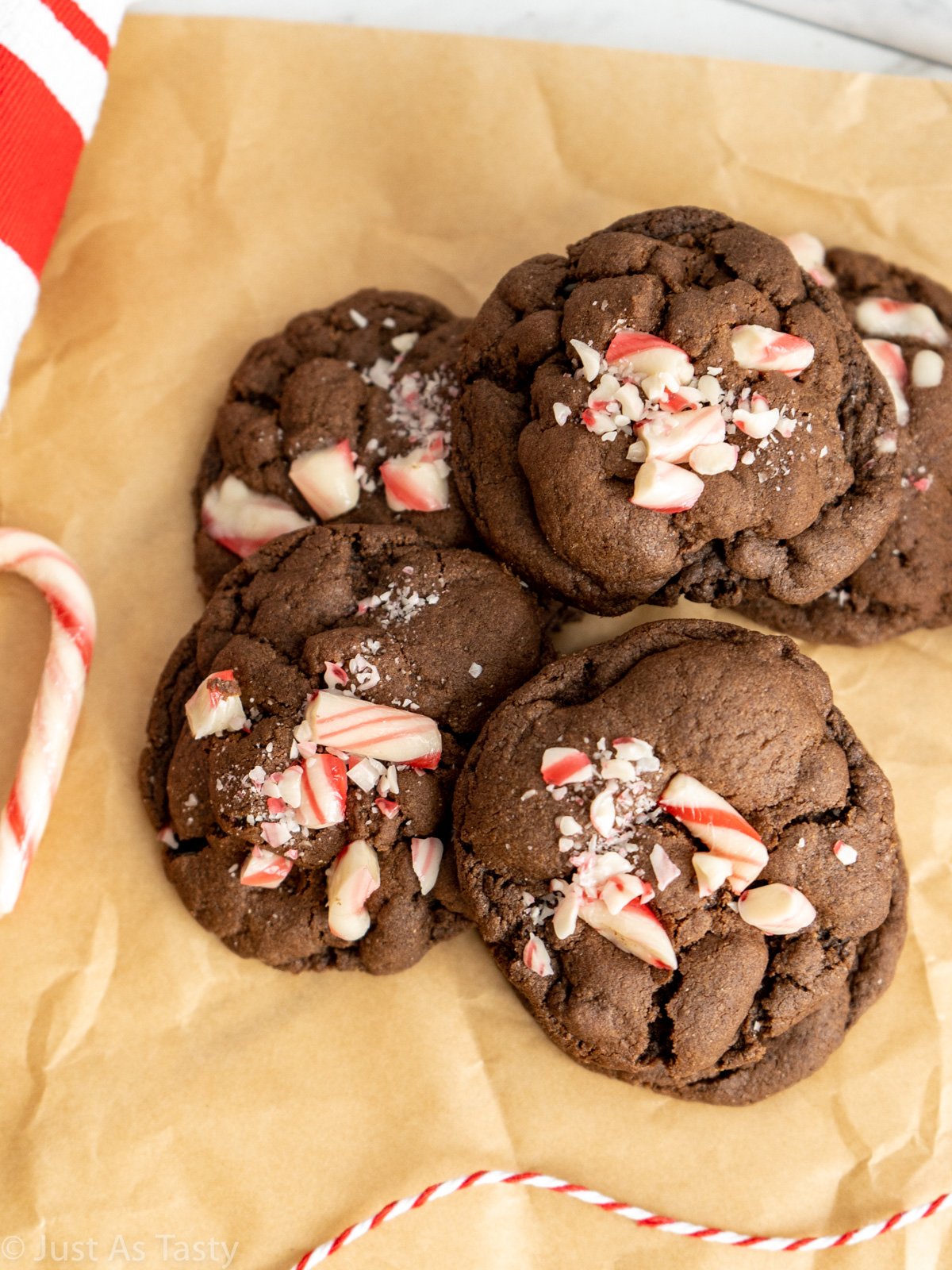 Chocolate cookies topped with crushed candy canes on brown parchment paper.