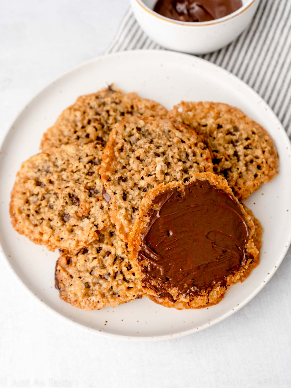 Oatmeal lace cookies on a plate. One is topped with melted chocolate.  