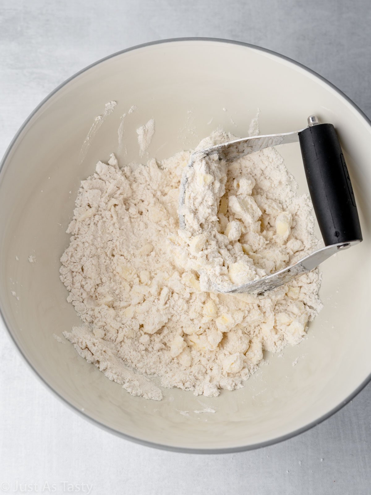 Pastry blender in mixing bowl with dry ingredients and pieces of butter.