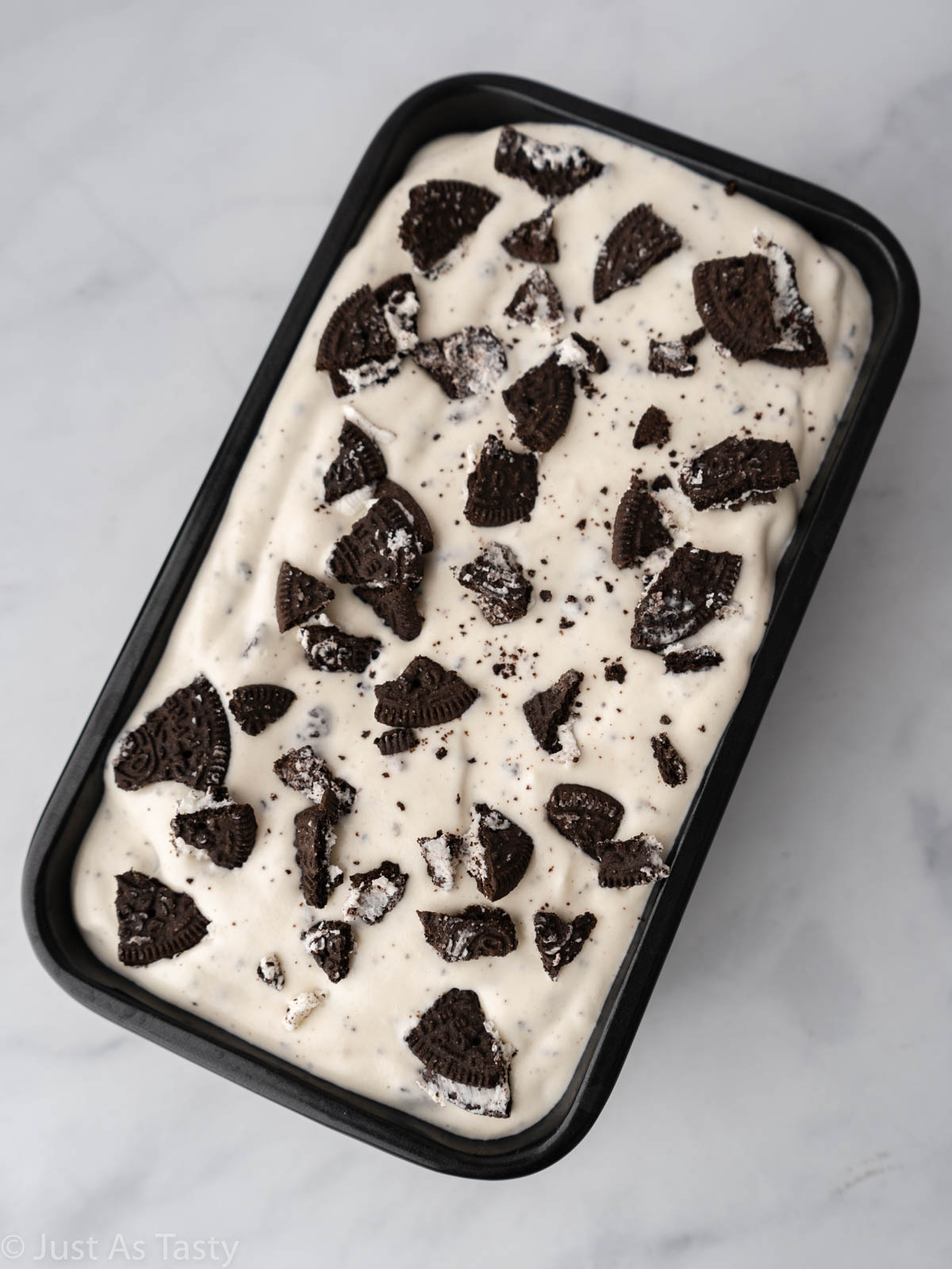 Ice cream topped with Oreo pieces in a loaf pan.