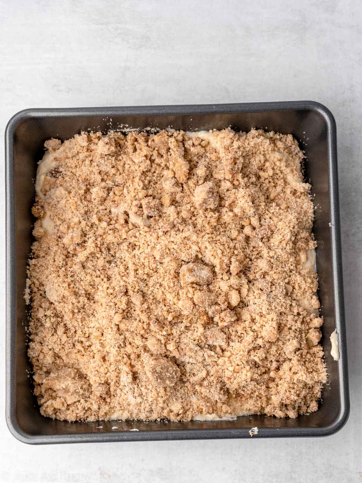 Cake batter topped with streusel in a square baking pan.