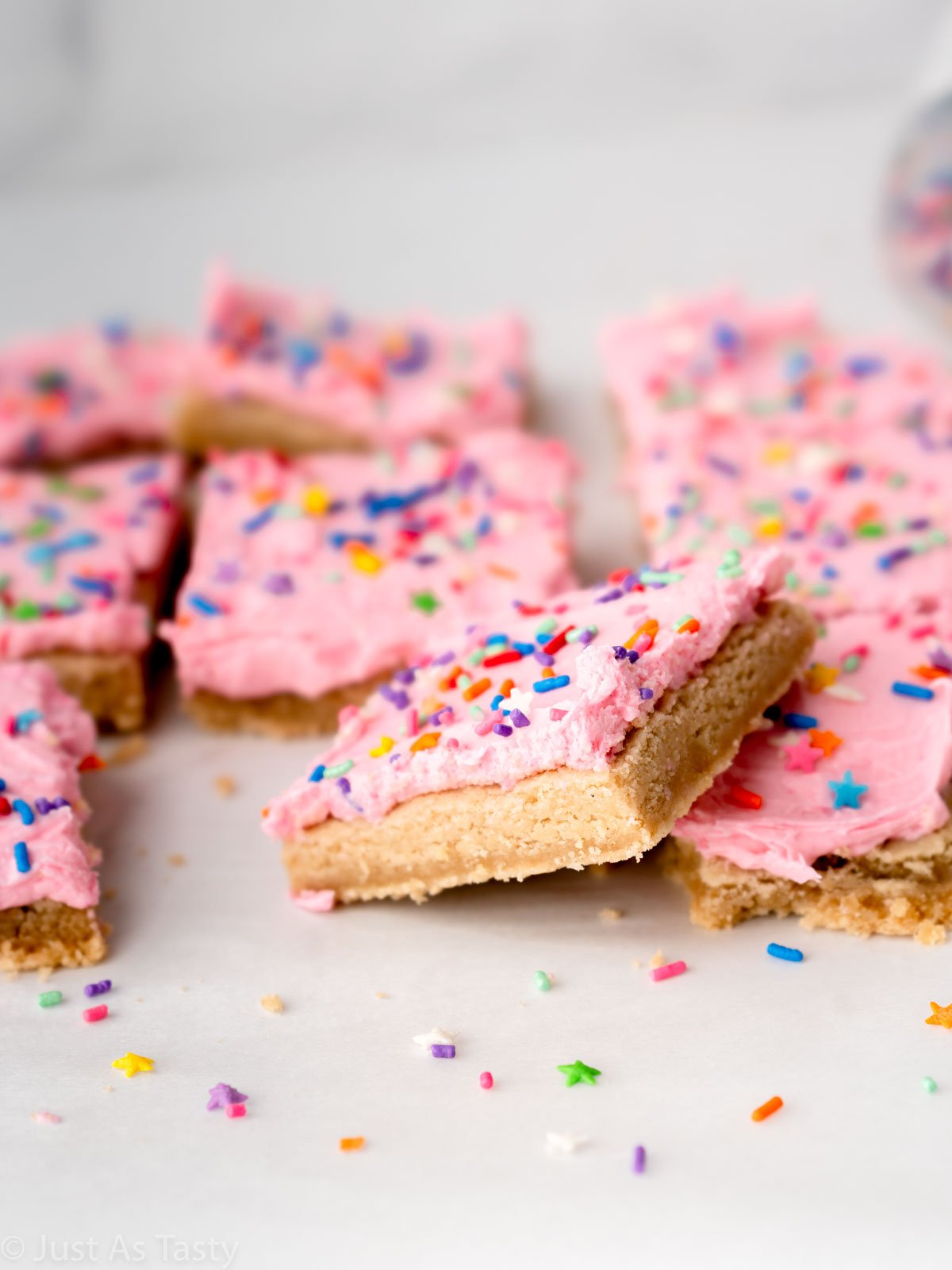 Pink frosted sugar cookie cake bars on parchment paper. 