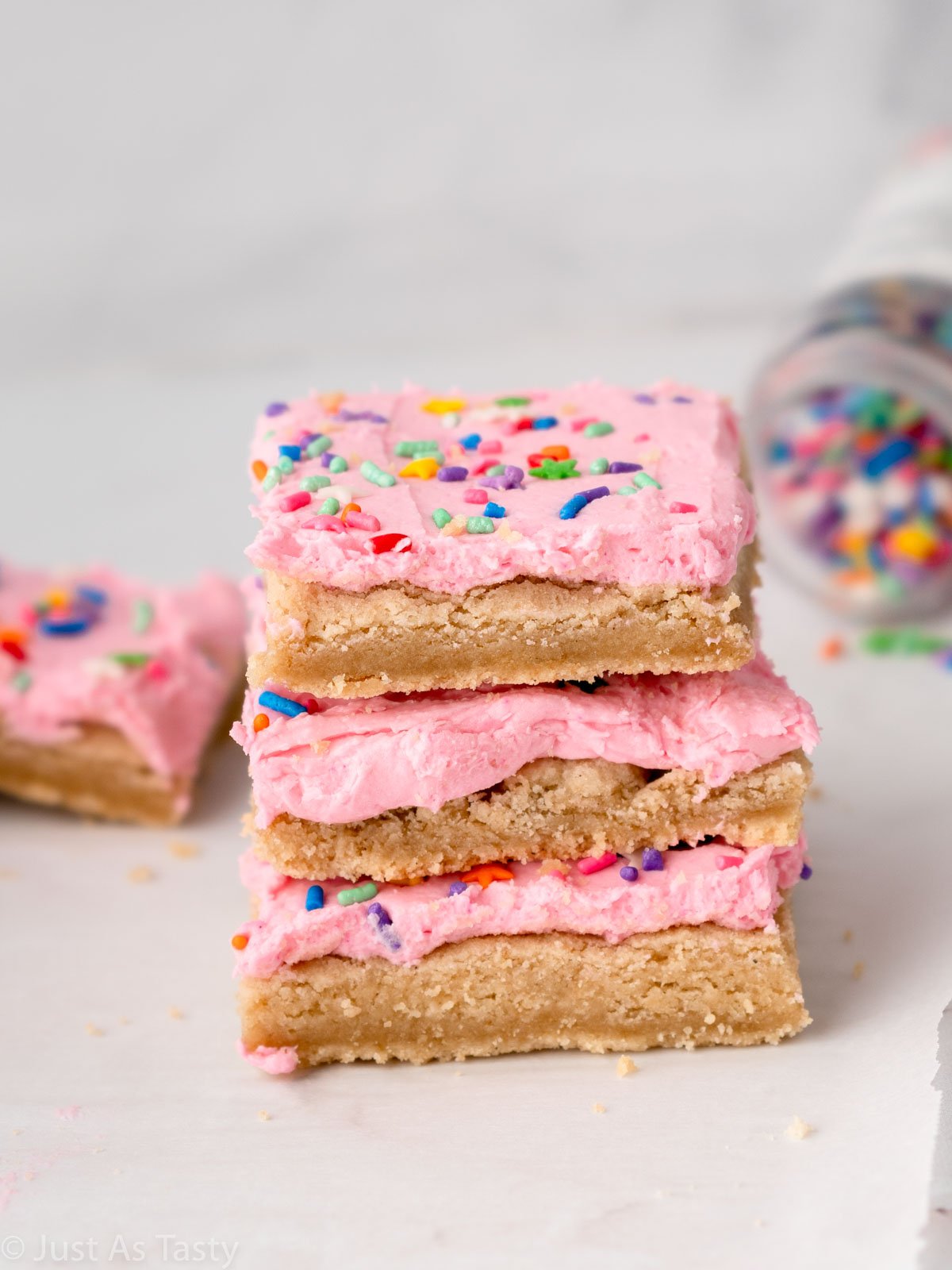 Stack of three pink frosted sugar cookie cake bars. 