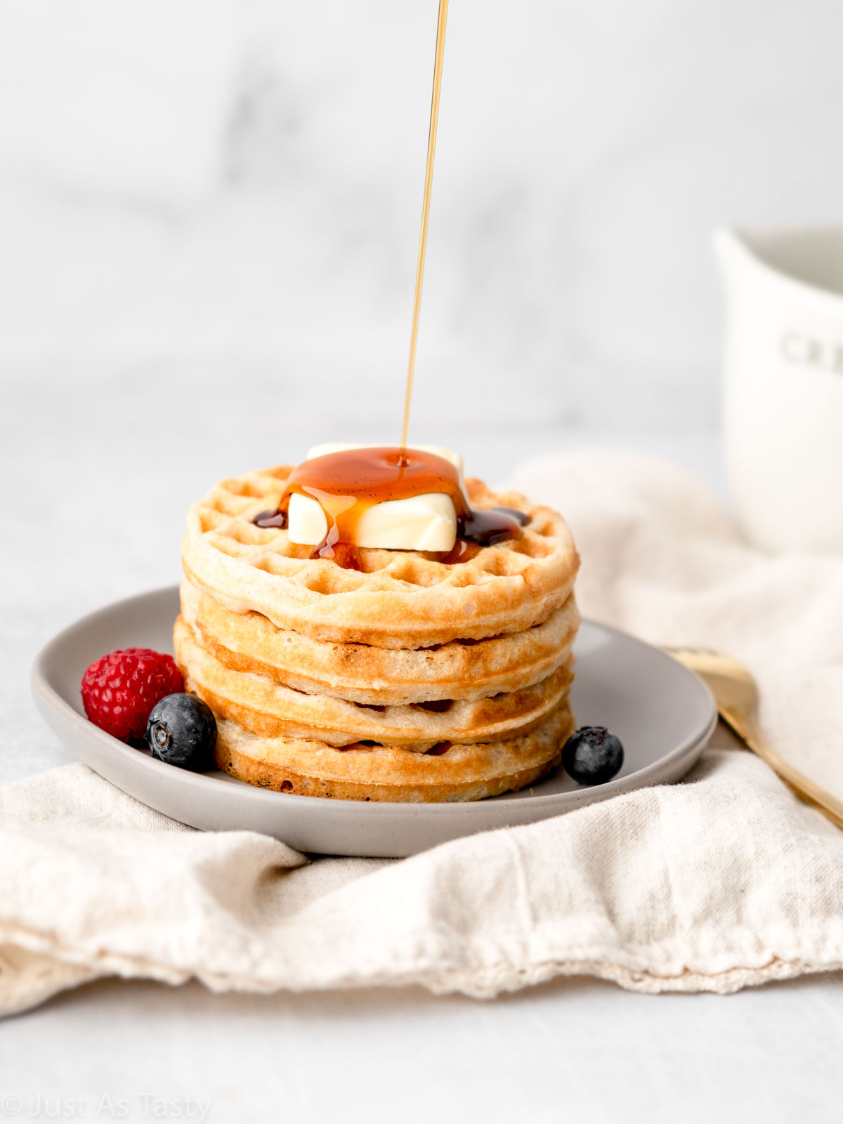 Syrup being poured onto stack of waffles. 