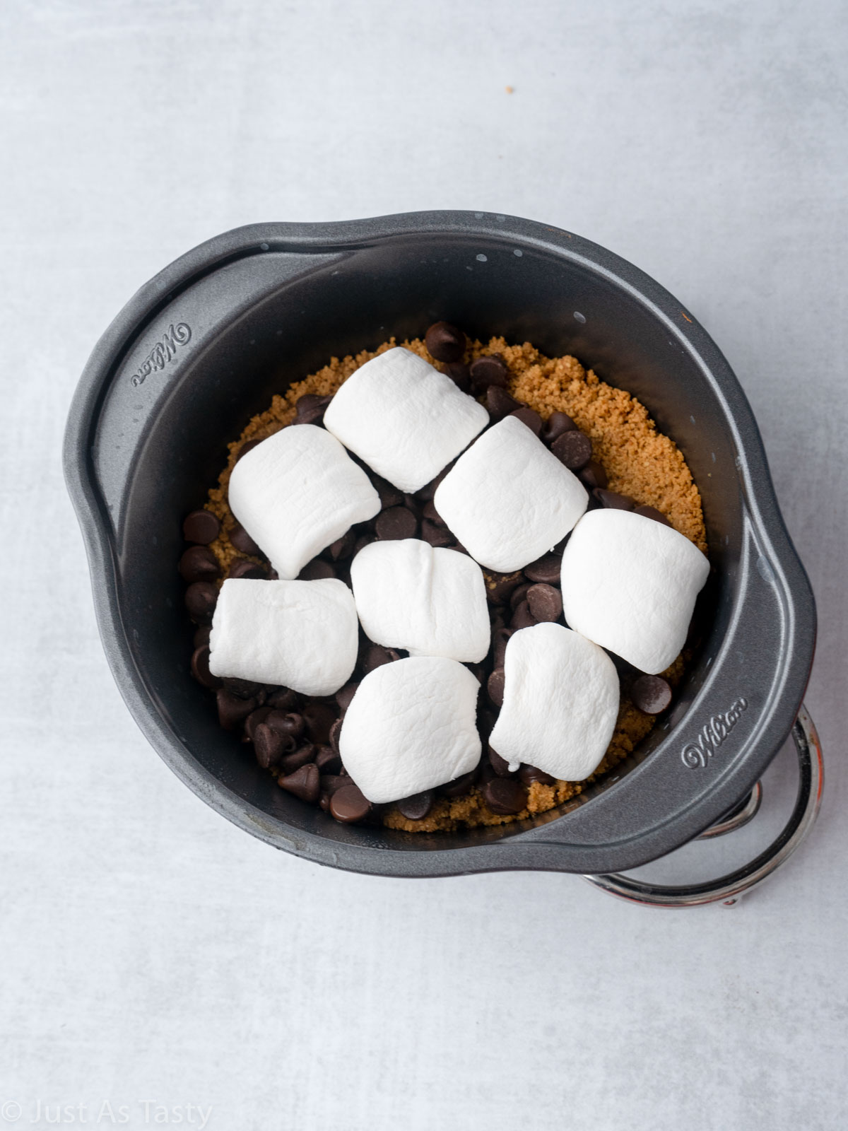 Graham cracker crust topped with chocolate chips and marshmallows in a cake pan.
