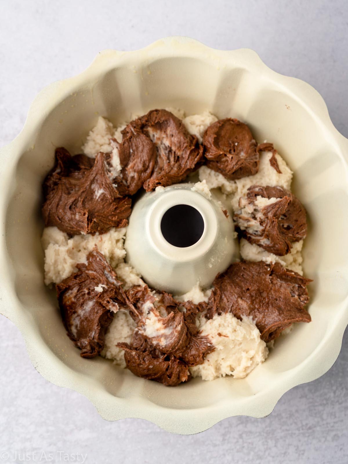 Scoops of chocolate and vanilla cake batter in a bundt pan. 