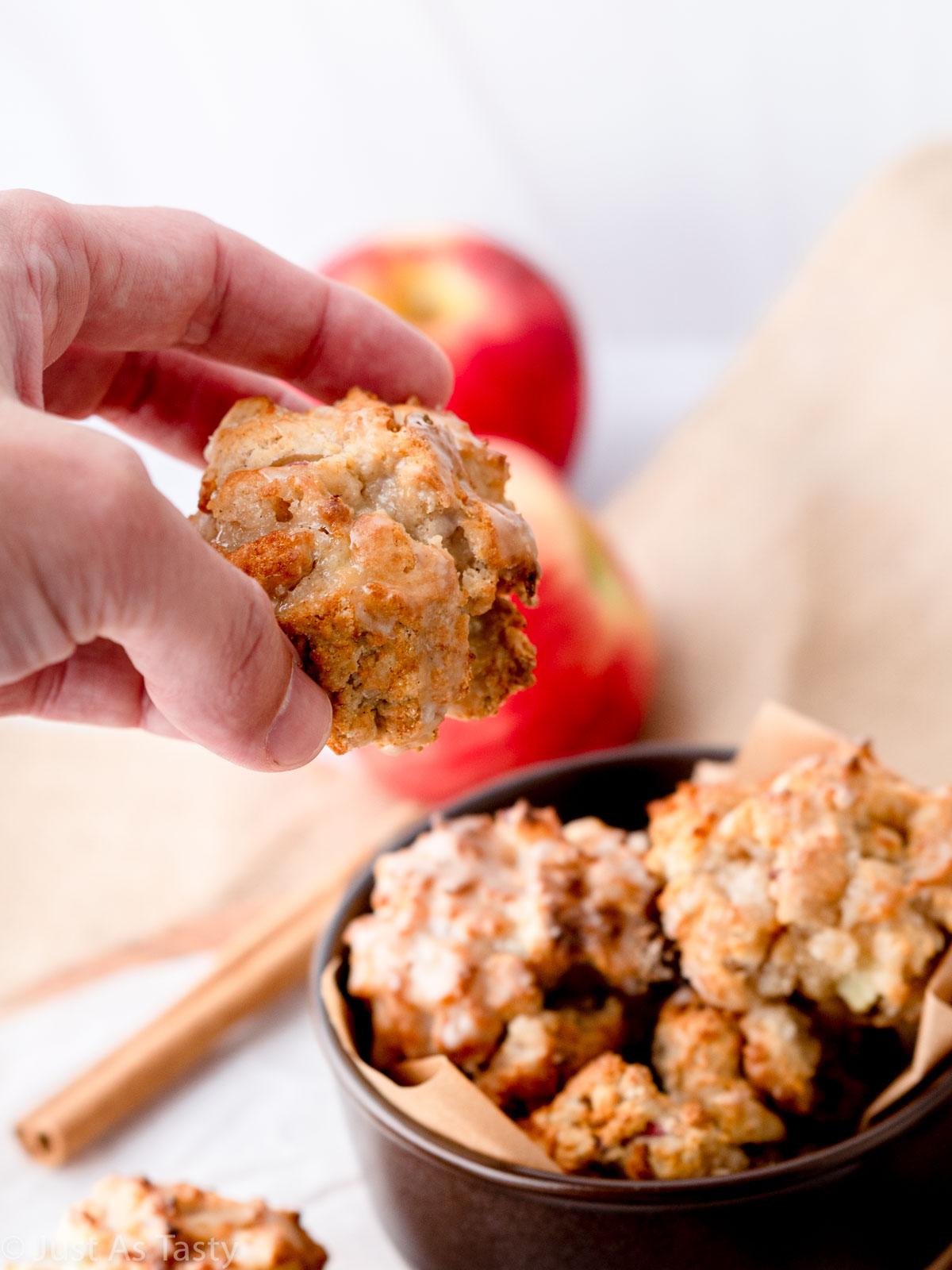 Hand picking up a glazed apple fritter out of a bowl.