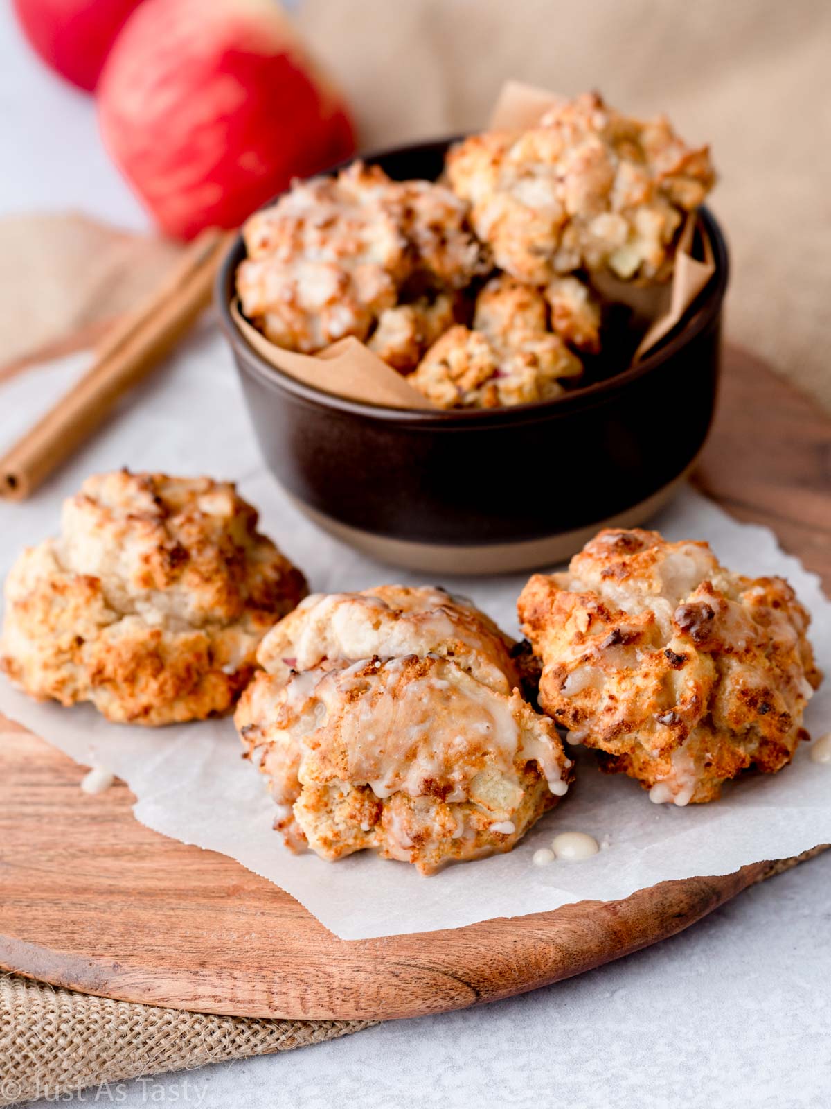 Glazed apple fritters in a bowl and on parchment paper.