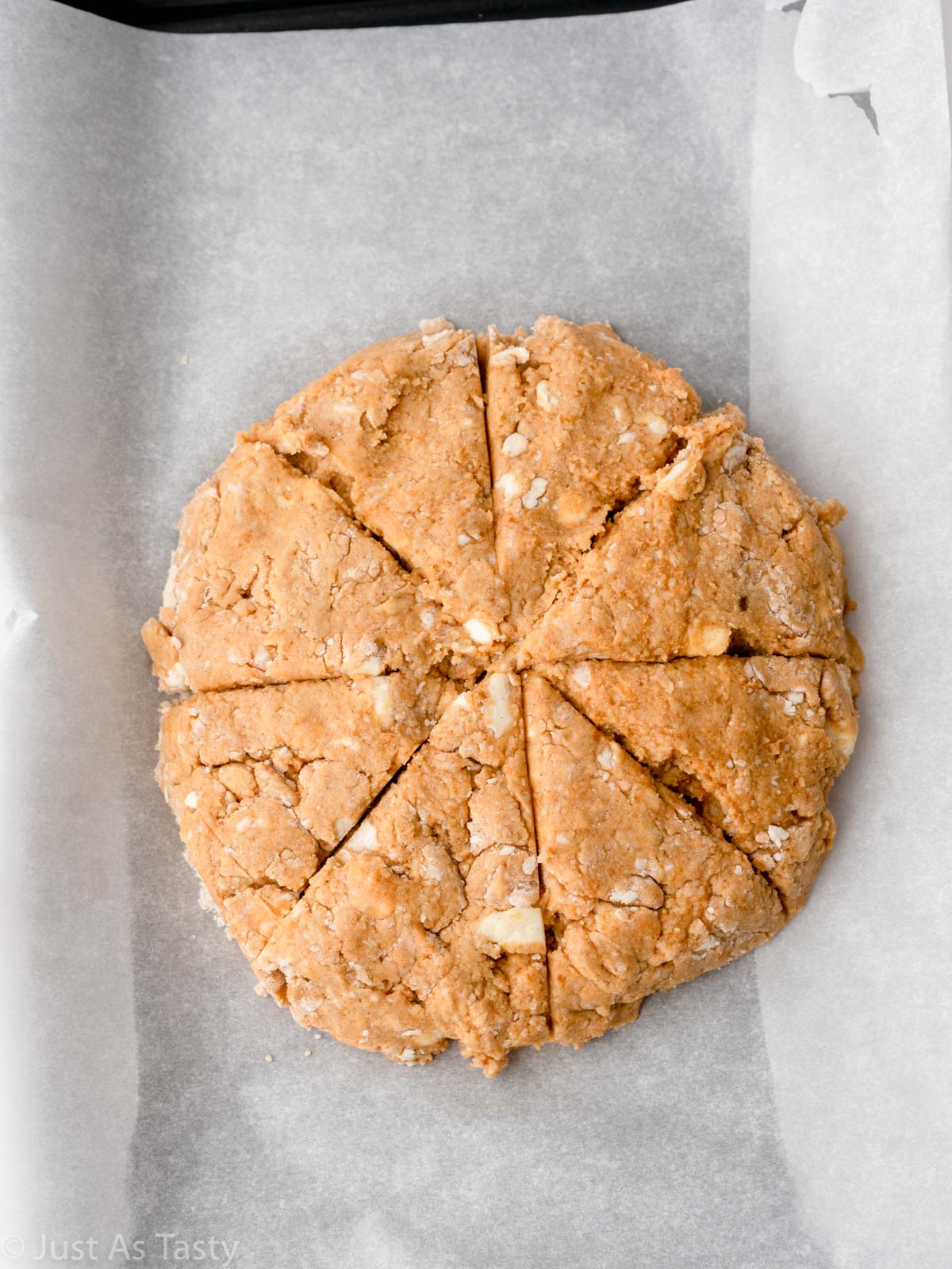 Pumpkin scone dough shaped into a disc on a lined baking sheet. 