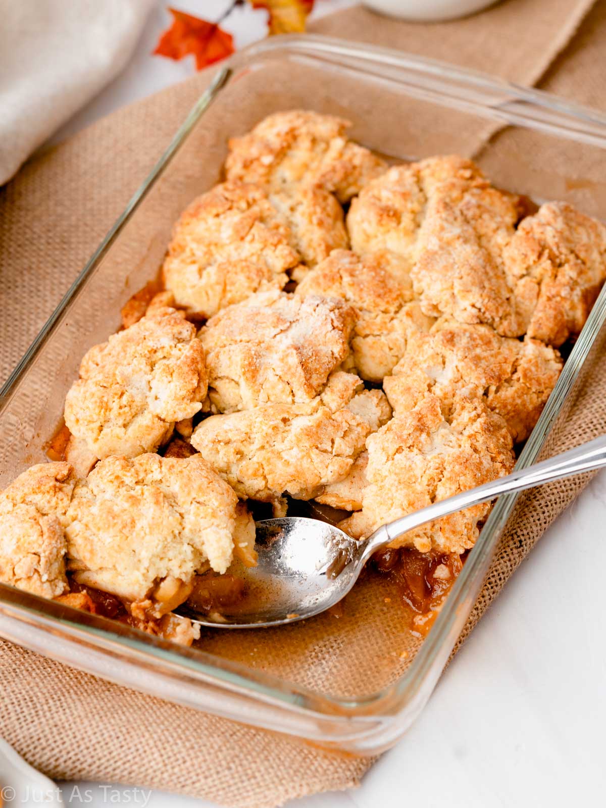 Gluten free apple cobbler in a glass dish with a serving spoon.