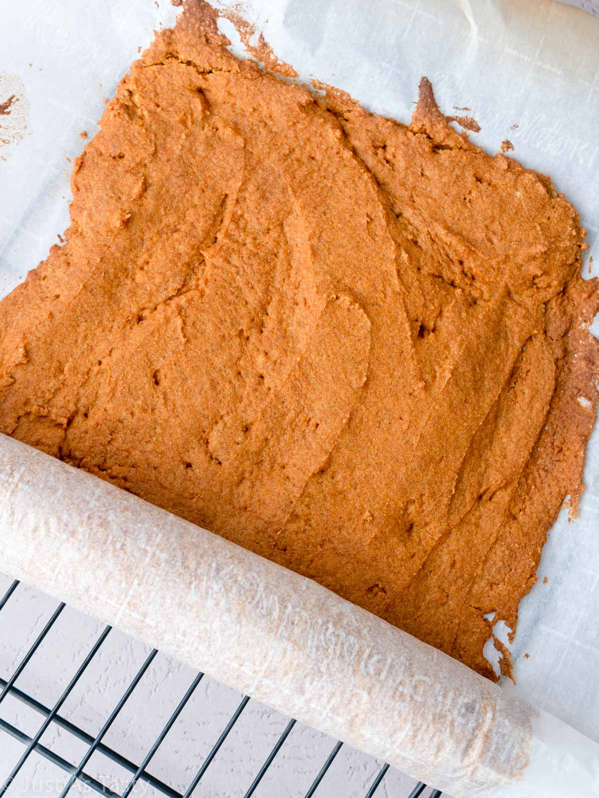 Baked pumpkin cake being rolled in parchment. 