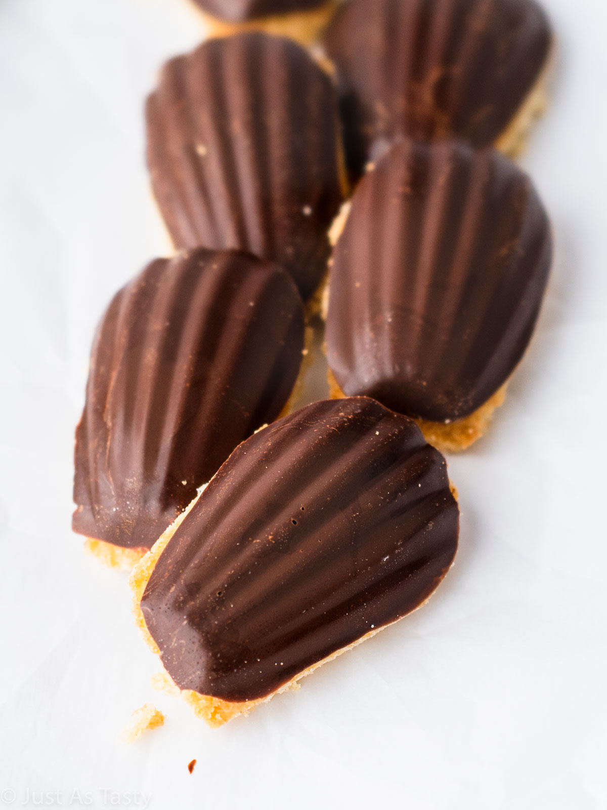 Chocolate dipped madeleines on a white surface.