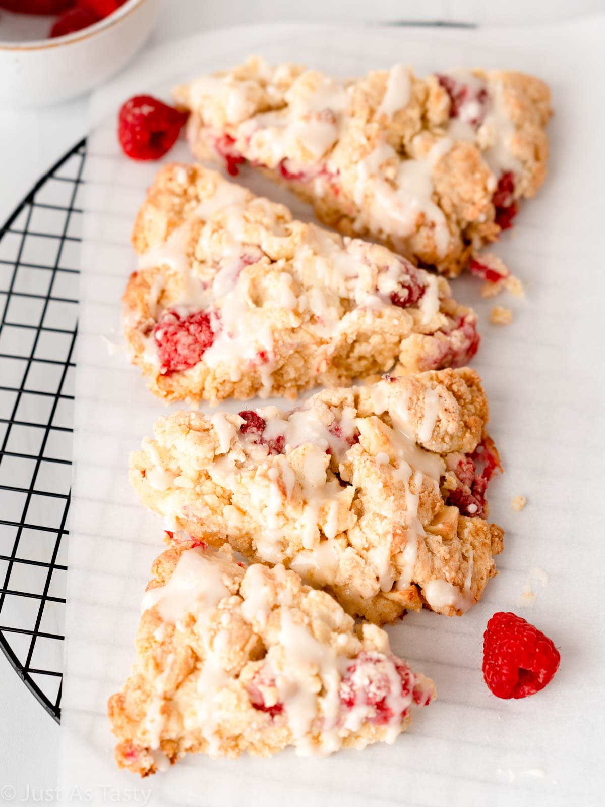 Four glazed white chocolate raspberry scones on parchment paper. 