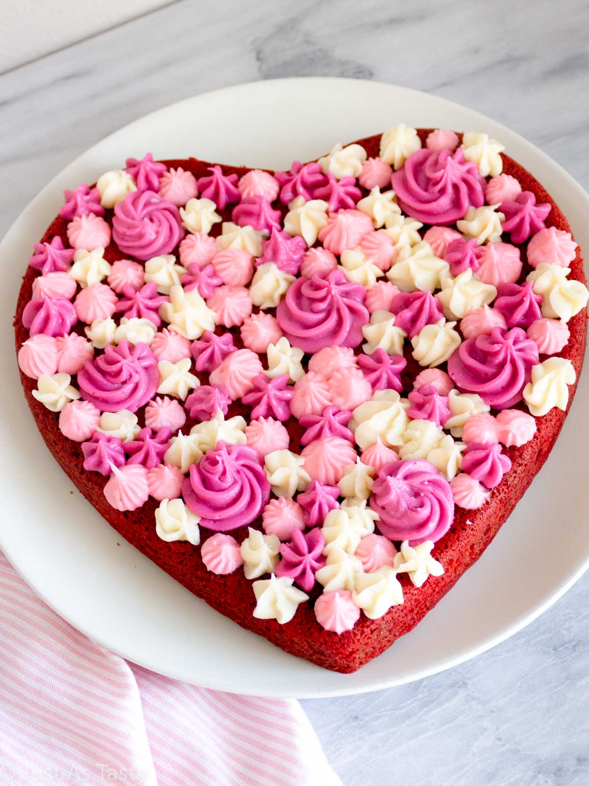 Heart shaped gluten free red velvet cake with pink and white piped cream cheese frosting on top.