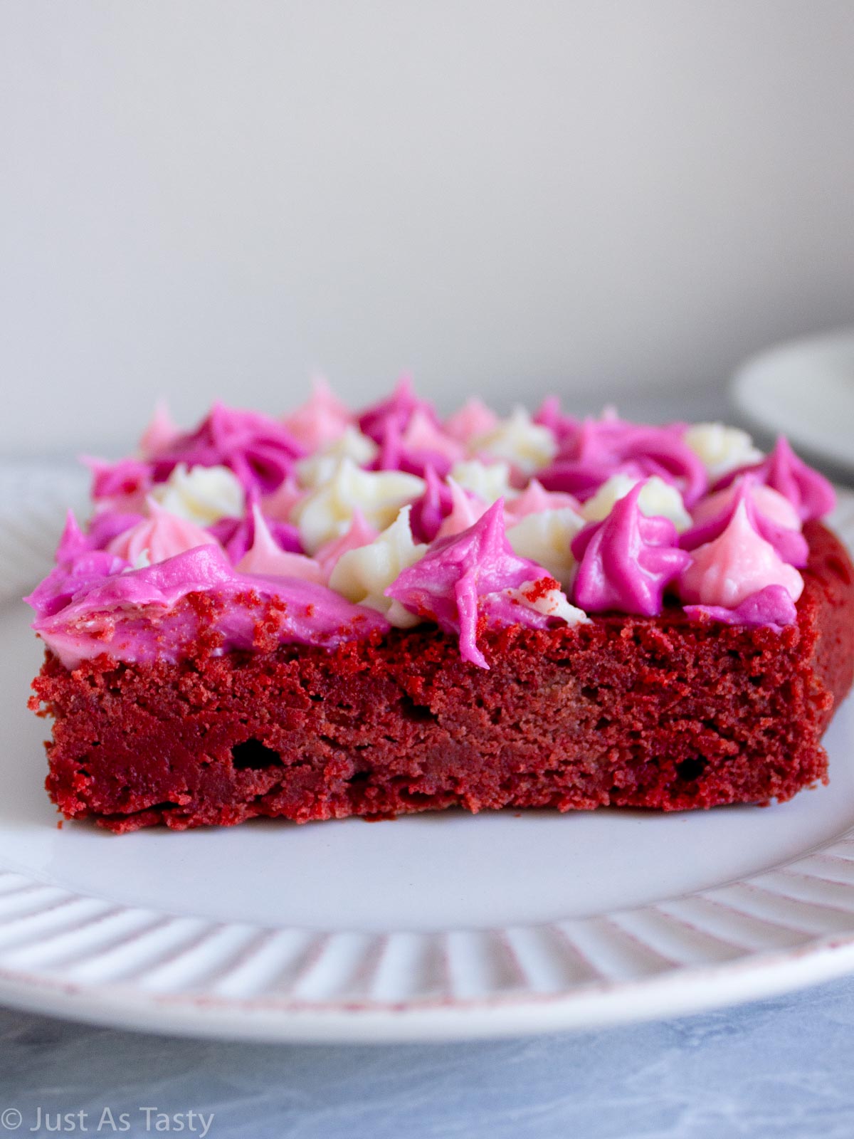 Close-up of a slice of gluten free red velvet cake with piped frosting on top.