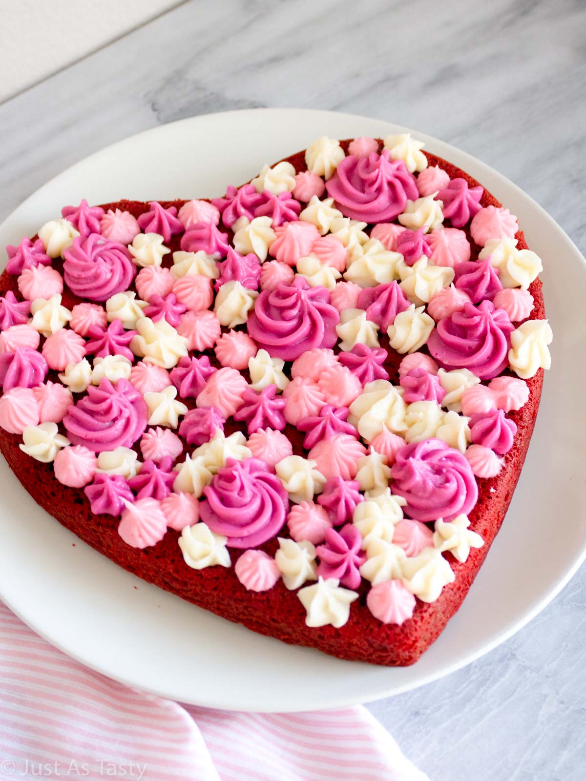 Heart shaped gluten free red velvet cake with pink and white piped frosting on top.