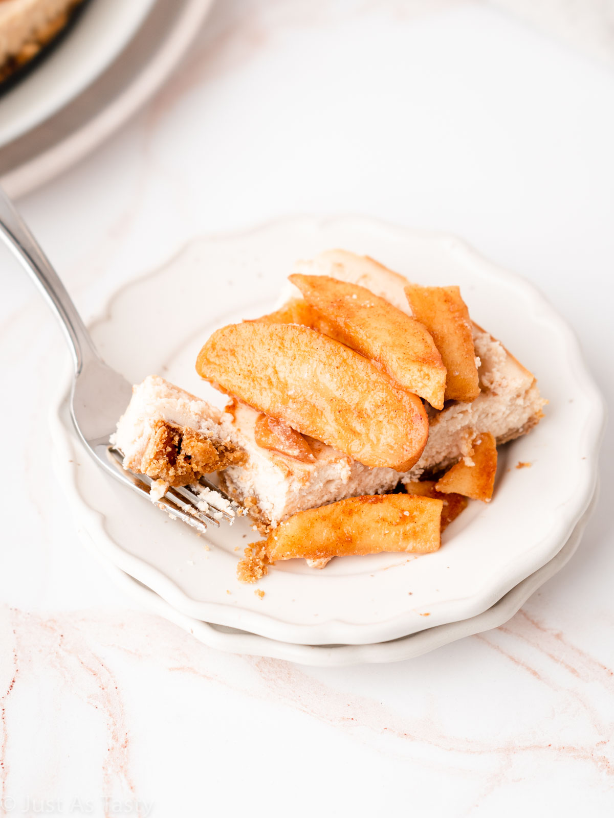 Apple pie cheesecake on a plate with a bite cut out on a fork.