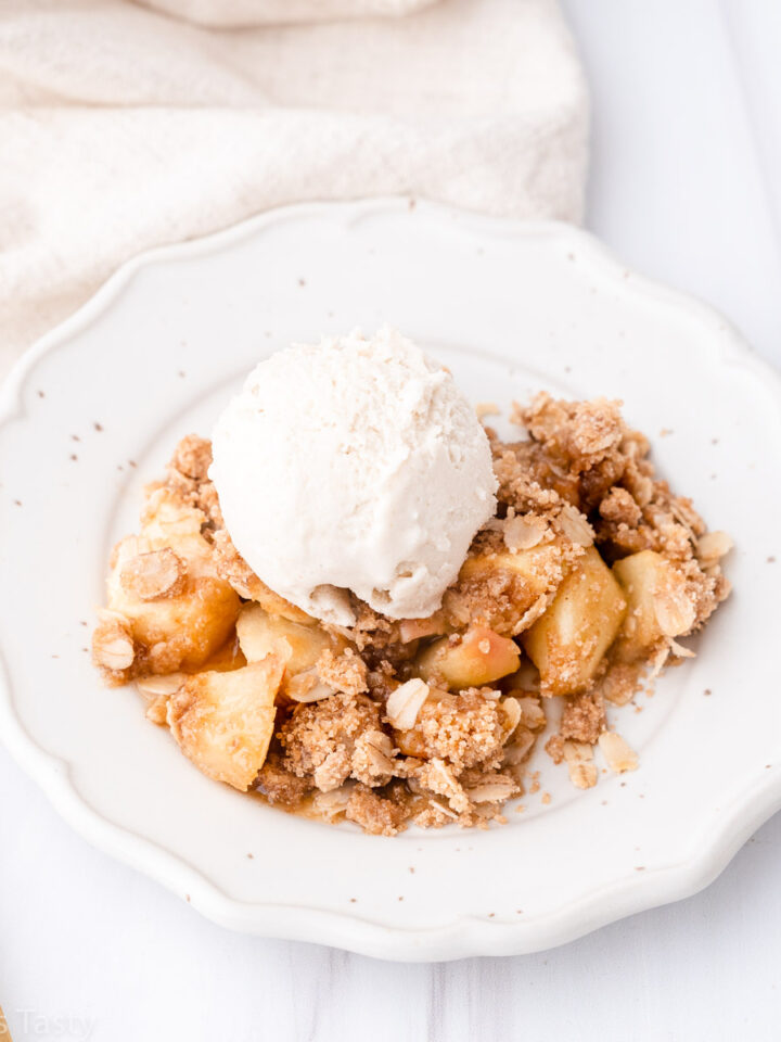 Gluten free apple crisp on a white plate topped with a scoop of vanilla ice cream.